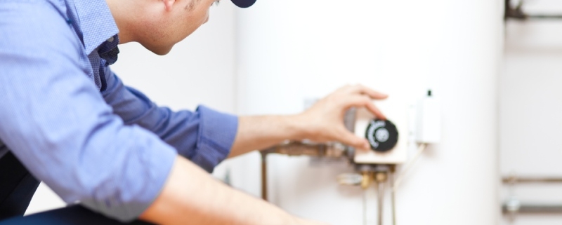 Plumber crouching to drain a hot water heater in property