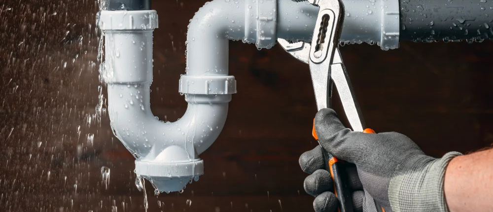 Close up of a plumber fixing a water leak in a sink drain siphon pipe.