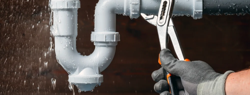 Close up of a plumber fixing a water leak in a sink drain siphon pipe.