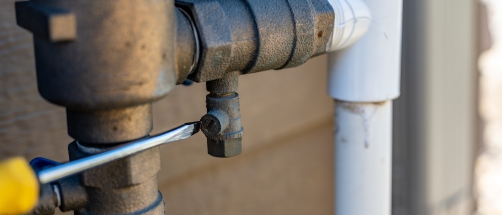 Using a flathead screwdriver to close the test cock when winterizing backflow preventer
