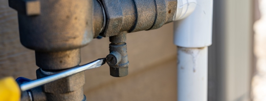 Using a flathead screwdriver to close the test cock when winterizing backflow preventer