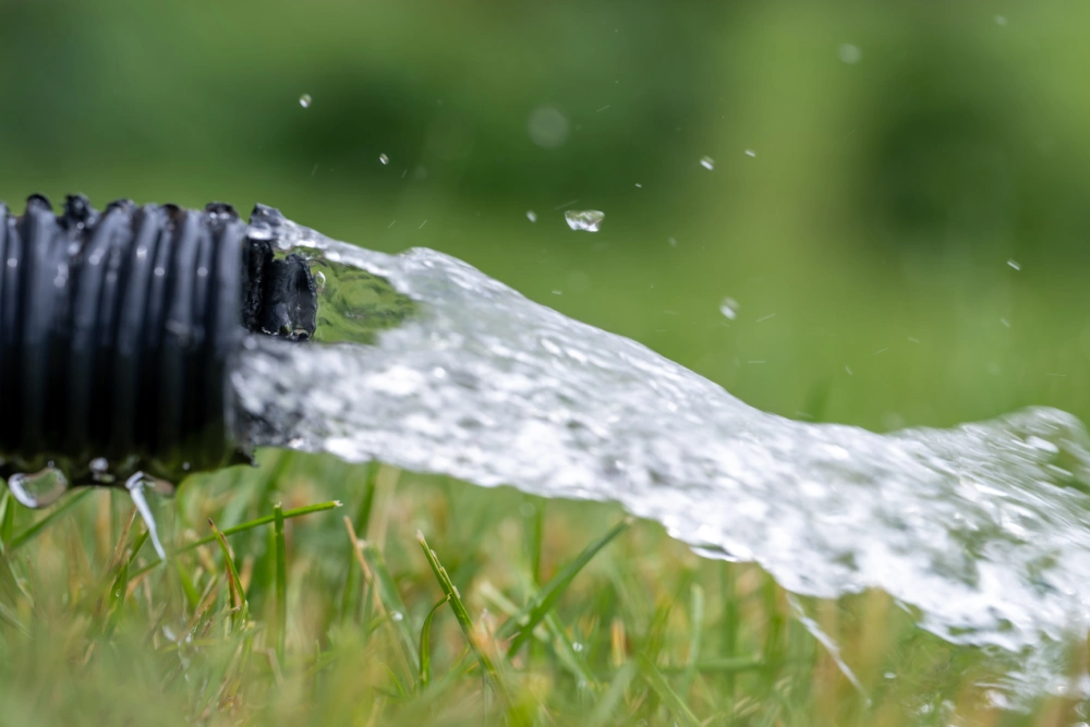 Residential sump pump drain line discharging water into grass yard