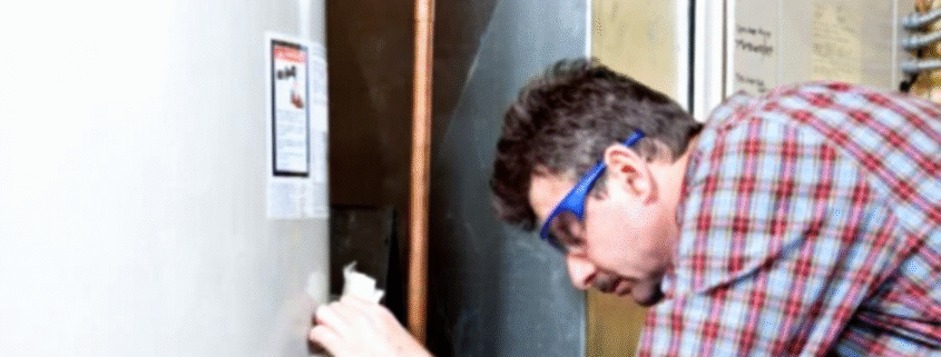 A technician is repairing a residential electric water heater in a utility room.